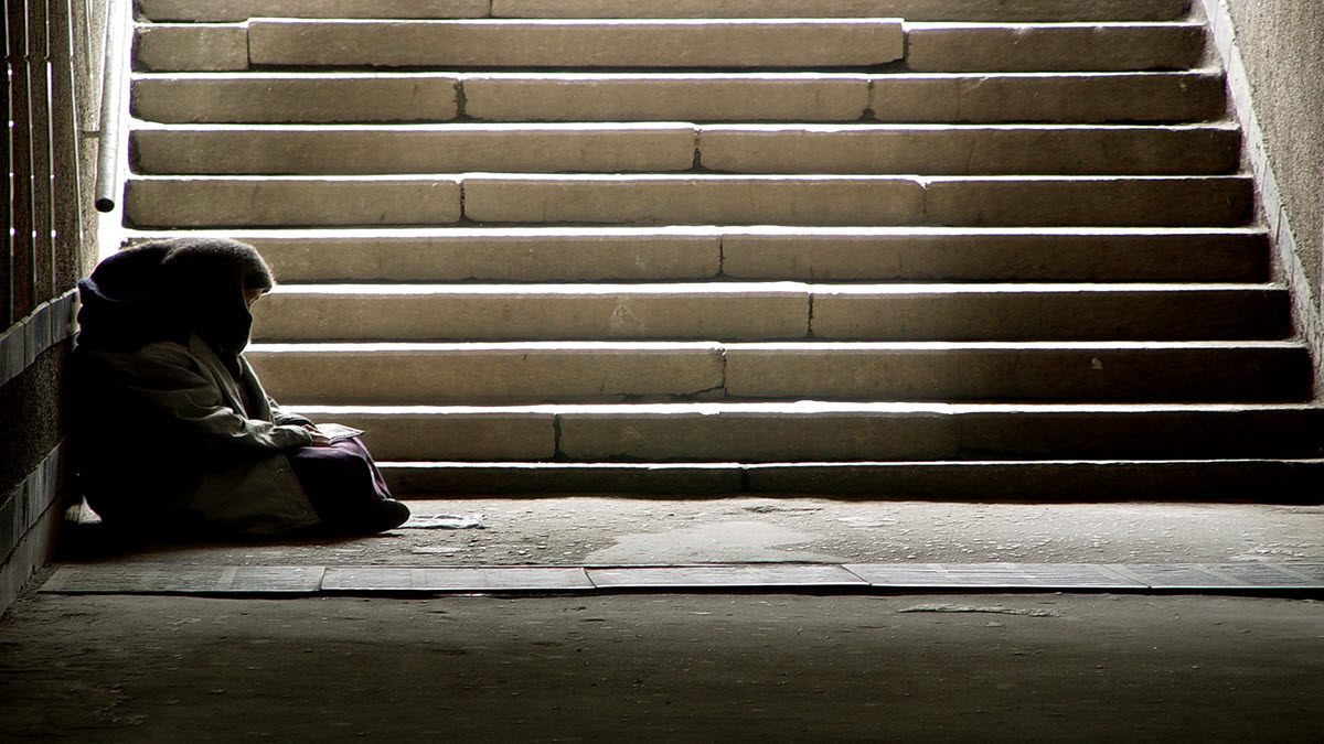 A person experiencing homelessness Una persona sin hogar sentada en la base de una escalera.